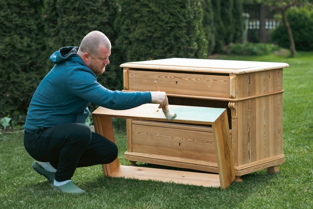 Man painting a wooden furniture while sitting with hir dog in the garden. DIY concept.